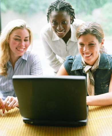 Three women sharing laptop computer at workplace