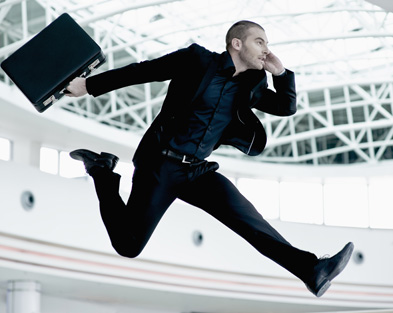 Young businessman jumping in midair with cell phone and briefcase